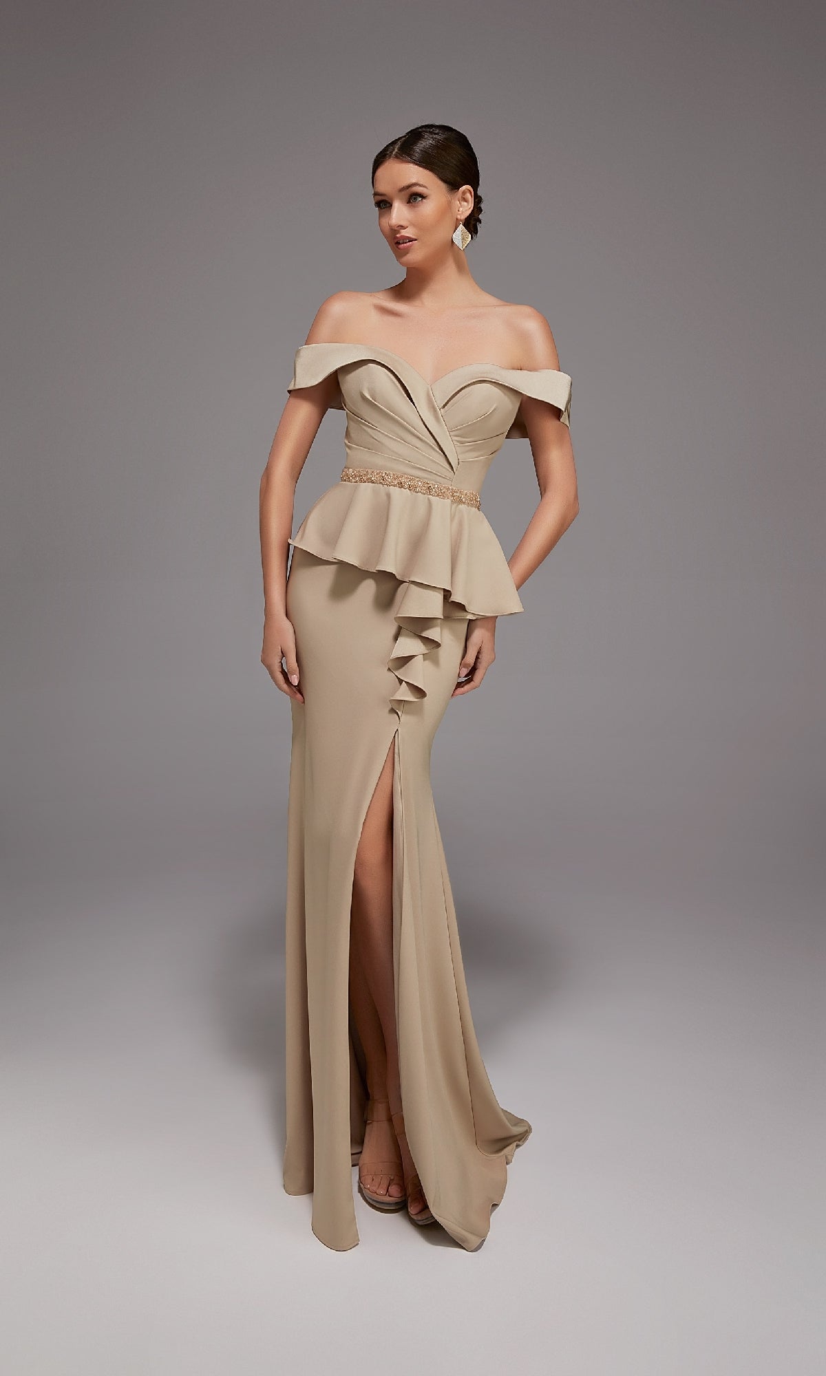 A woman poses against a plain gray background wearing the Alyce 27829 long formal dress, featuring an off-the-shoulder neckline, peplum waist, front slit, and ruffle detail—ideal for special occasions.